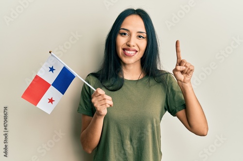 Young hispanic girl holding panama flag smiling with an idea or question pointing finger with happy face, number one