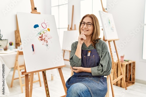 Middle age artist woman at art studio looking confident at the camera smiling with crossed arms and hand raised on chin. thinking positive.