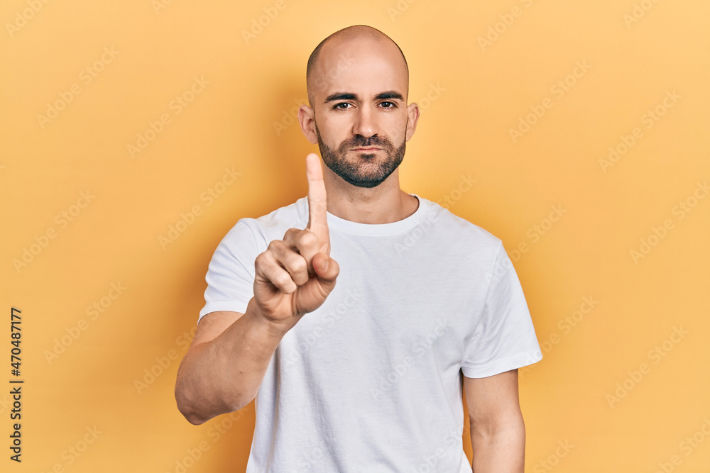 Young bald man wearing casual white t shirt pointing with finger up and angry expression, showing no gesture Young bald man wearing casual white t shirt pointing with finger up and angry expression, showing no gesture