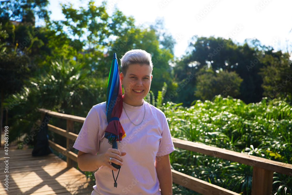 Fototapeta premium non-binary gender non-binary androgynous person with a gay pride umbrella. He is smiling and looking at the camera. Non-binary and androgynous concept. Diversity concept.
