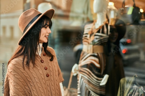 Brunette woman wearing winter hat looking at shop window outdoors at the city