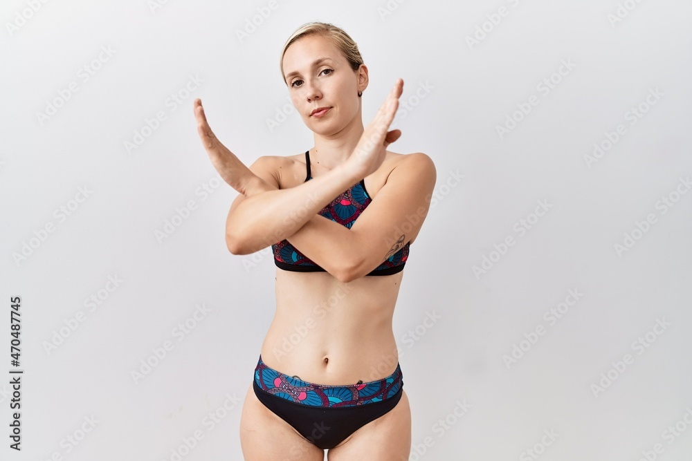 Young blonde woman wearing sporty bikini over isolated background rejection expression crossing arms doing negative sign, angry face Young blonde woman wearing sporty bikini over isolated background rejection expression crossing arms doing negative sign, angry face