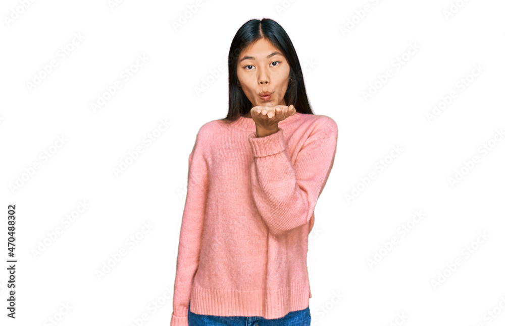 Beautiful young asian woman wearing casual winter sweater looking at the camera blowing a kiss with hand on air being lovely and sexy. love expression. Beautiful young asian woman wearing casual winter sweater looking at the camera blowing a kiss with hand on air being lovely and sexy. love expression.