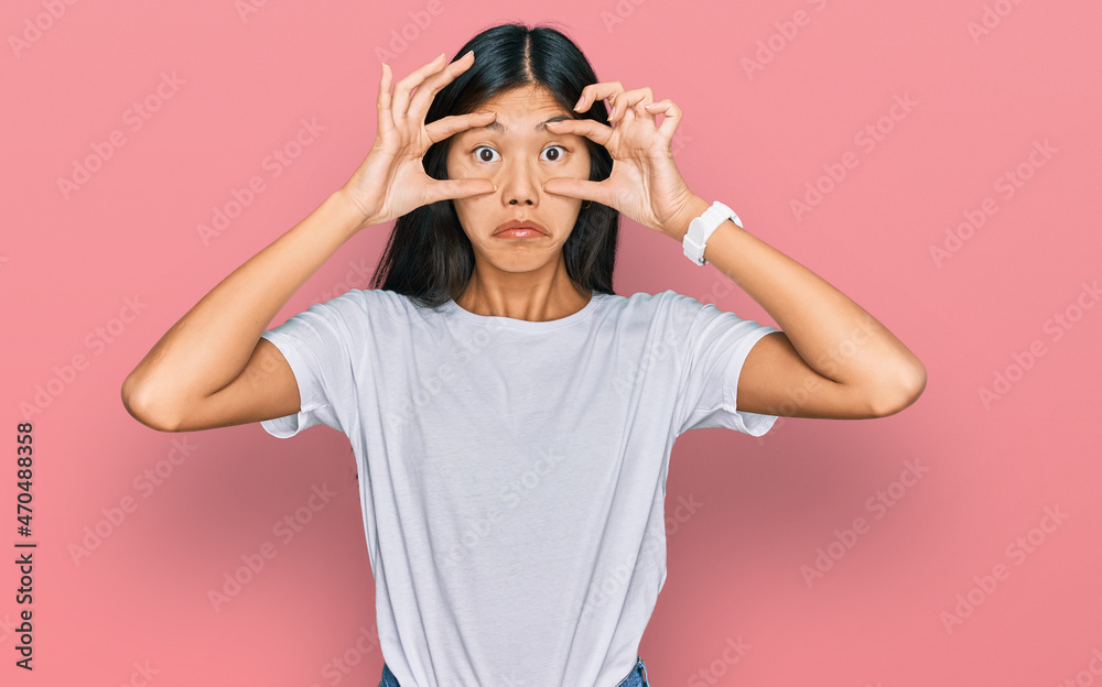 Beautiful young asian woman wearing casual white t shirt trying to open eyes with fingers, sleepy and tired for morning fatigue Beautiful young asian woman wearing casual white t shirt trying to open eyes with fingers, sleepy and tired for morning fatigue