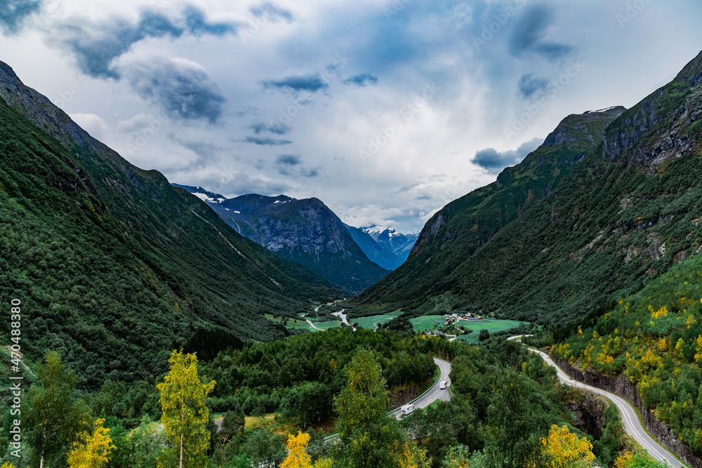 View from the road on a small village hidden in the valley between beautiful Norwegian mountains against  dramatic cloudy sky