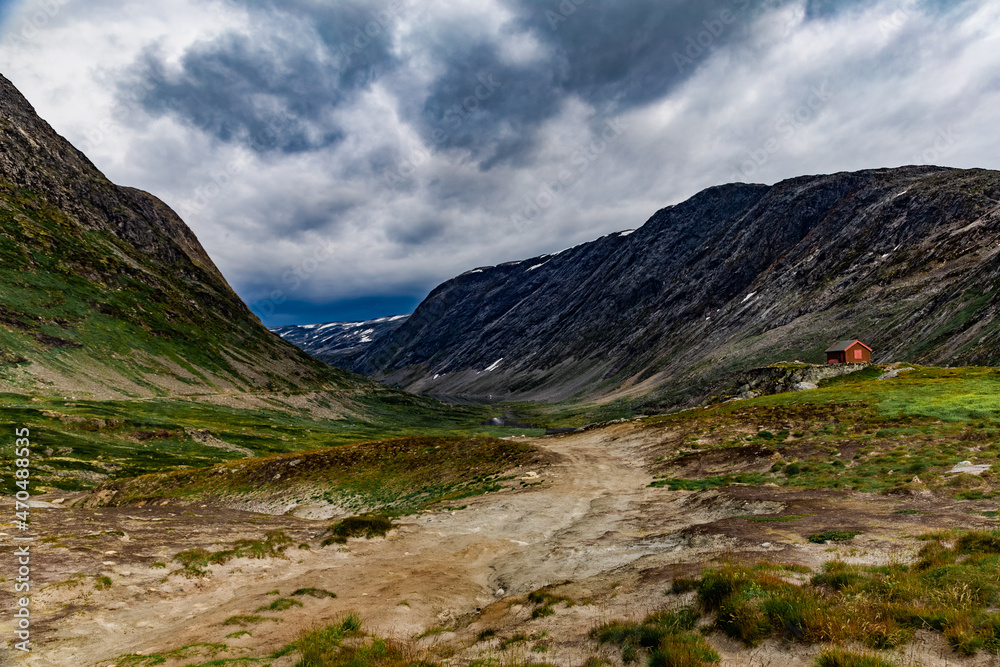 Energetic view on the rural road, small house and mountains against dramatic sky