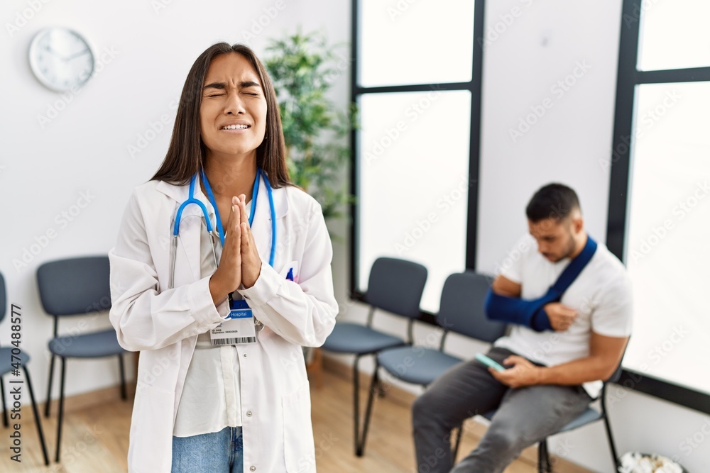 Young asian doctor woman at waiting room with a man with a broken arm begging and praying with hands together with hope expression on face very emotional and worried. begging. Young asian doctor woman at waiting room with a man with a broken arm begging and praying with hands together with hope expression on face very emotional and worried. begging.