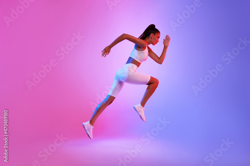 Fototapeta Naklejka Na Ścianę i Meble -  Determined Sporty Woman Running In Mid-Air Over Neon Background, Side-View