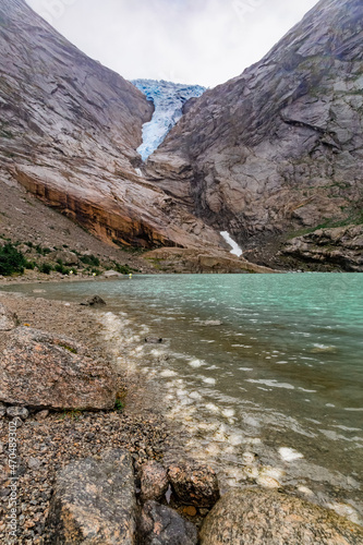 Scenic view on ice pieces from the glacier, Briksdal glacier, lake and Norwegian mountains against cloudy dramatic sky