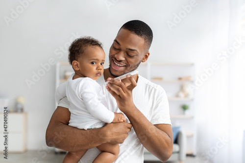 Modern Technologies And Babies. Father Holding Infant Child And Talking On Speakerphone