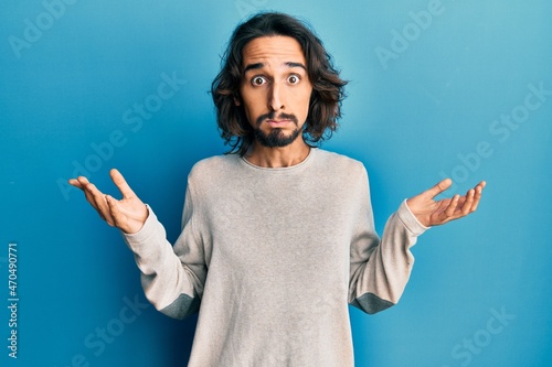 Young hispanic man wearing casual clothes clueless and confused with open arms, no idea and doubtful face.