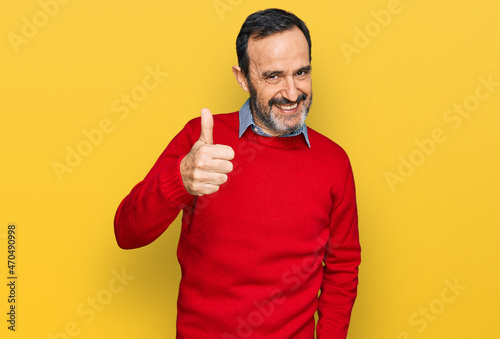 Middle age hispanic man wearing casual clothes doing happy thumbs up gesture with hand. approving expression looking at the camera showing success.