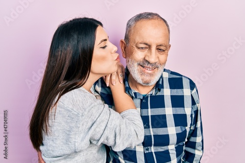 Young brunette woman and senior man standing over pink background. Daughter and father hugging and bonding together as happy family