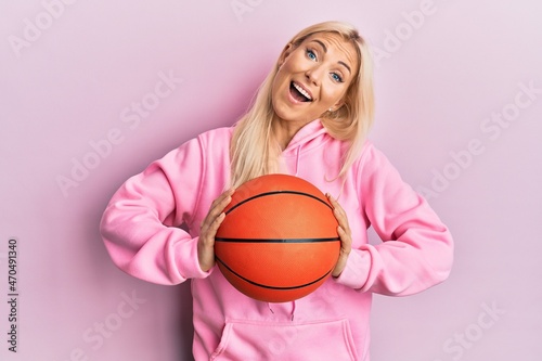 Young blonde woman holding basketball ball celebrating crazy and amazed for success with open eyes screaming excited.