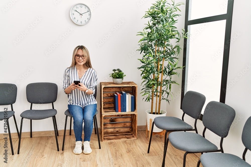 Fototapeta premium Young chinese woman using smartphone sitting on chair at waiting room
