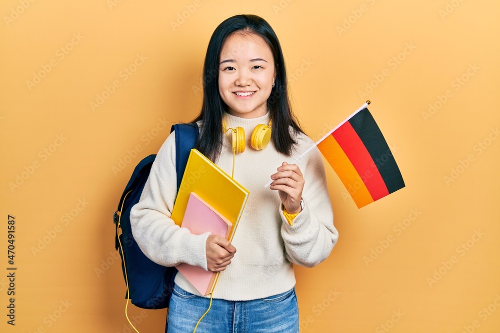 Young chinese girl exchange student holding germany flag smiling with a happy and cool smile on face. showing teeth. Young chinese girl exchange student holding germany flag smiling with a happy and cool smile on face. showing teeth.