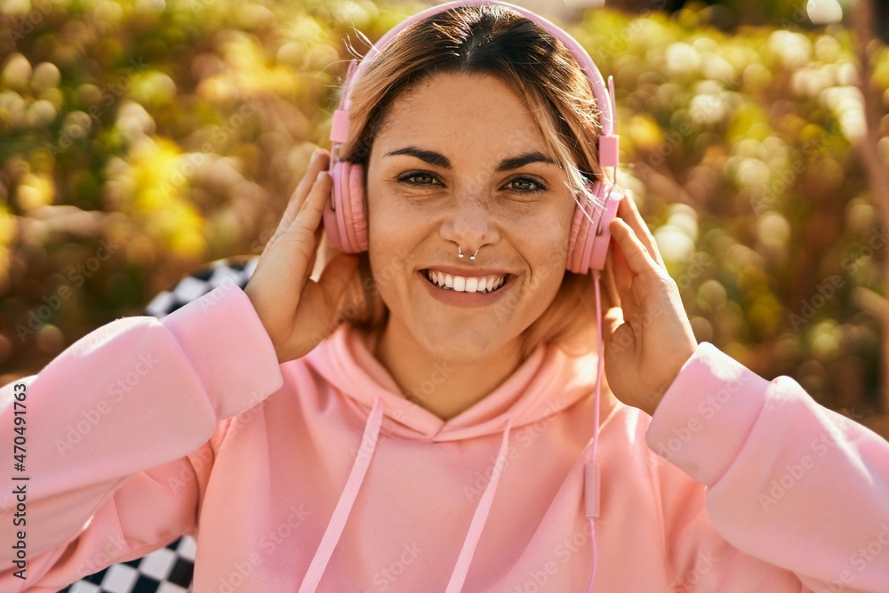 Young blonde skater girl smiling happy using headphones sitting at the park