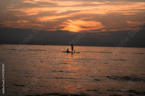 People on a SUP enjoying the beautiful orange sunset at lake Garda in italy 