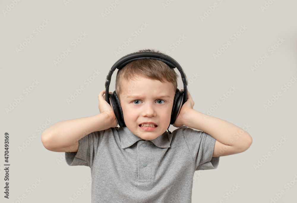 Preschooler boy in headphones with a sour face listening to terrible musi Preschooler boy in headphones with a sour face listening to terrible musi