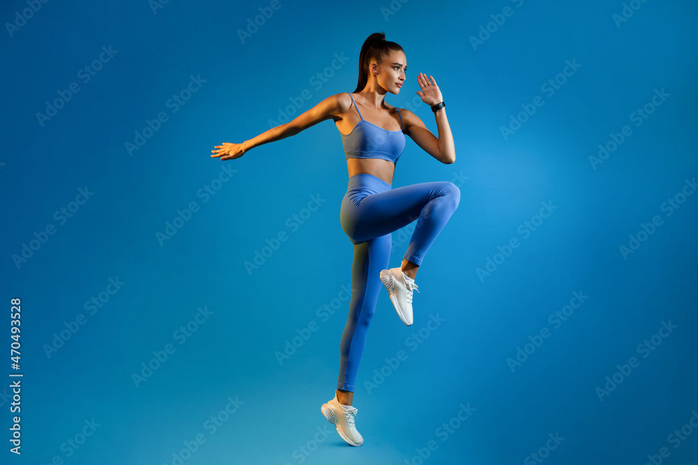 Female Athlete Jumping Exercising During Training Over Blue Studio Background
