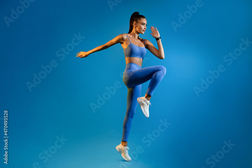 Fototapeta Naklejka Na Ścianę i Meble -  Female Athlete Jumping Exercising During Training Over Blue Studio Background