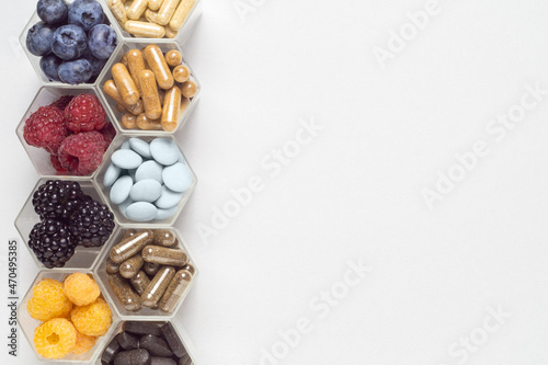 Fresh berries, pills and capsules in honeycomb like hexagonal jars photo