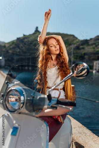 Young redhead woman relaxing near italian scooter. Sea on background © Nikolay
