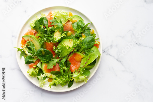 Salmon, avocado and assorted lettuce salad on white marble background