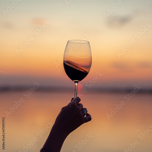Woman's hand holding a glass with red wine on a sunset background