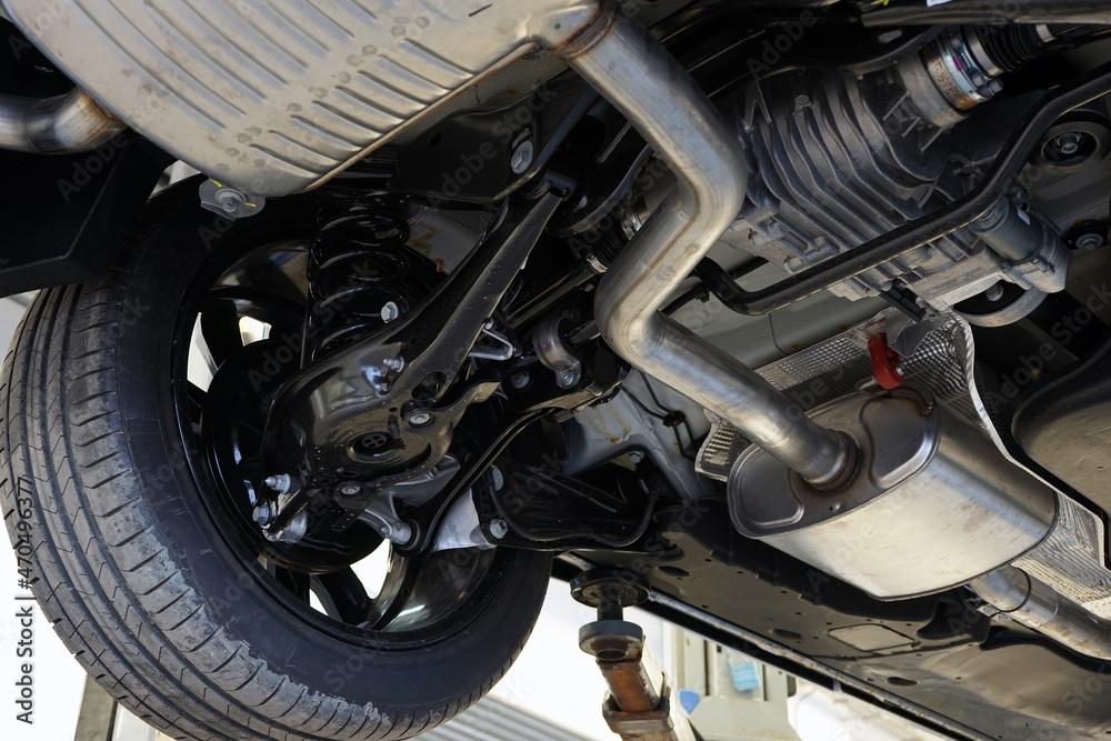 A modern car in a car service on a lift. Bottom view of the car. Details and structure of the suspension, elements of the exhaust system are visible. Car service and auto parts. Selected focus. A modern car in a car service on a lift. Bottom view of the car. Details and structure of the suspension, elements of the exhaust system are visible. Car service and auto parts. Selected focus.