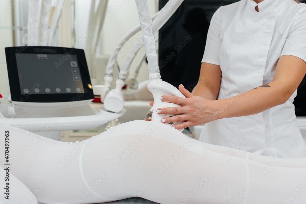 A young woman in a white suit, undergoing cosmetic LPG massage and laser  lipolysis, close-up. Cosmetic procedure, in a medical center.  Anti-cellulite procedures. Photos | Adobe Stock