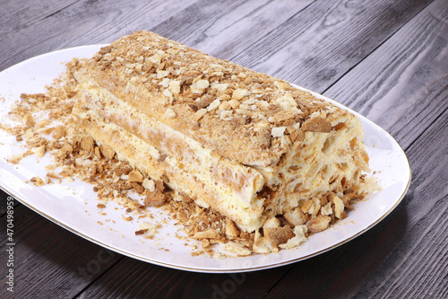 Puff pastry log cake on a white plate. Selective focus. Wooden background. Home pastry.Napaleon cake