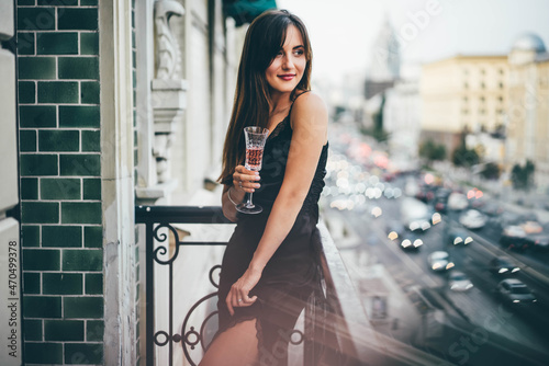 Fotografering Young woman in evening dress holding champagne glass at the balcony