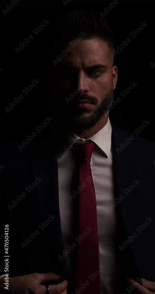 sexy young businessman with beard looking to side, arranging and closing suit, touching palms and posing in front of black background in studio sexy young businessman with beard looking to side, arranging and closing suit, touching palms and posing in front of black background in studio