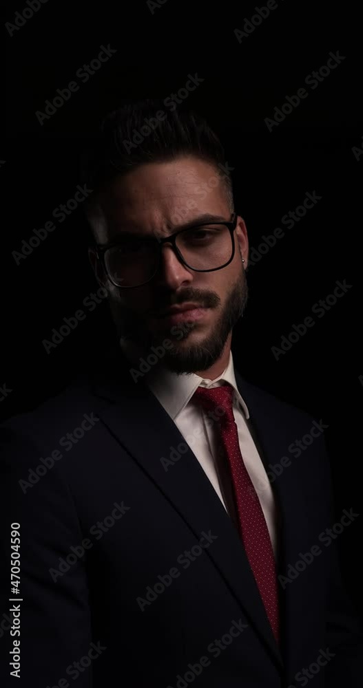 attractive elegant guy in suit wearing eyeglasses looking to side, pointing fingers in the air and confidently smiling on black background attractive elegant guy in suit wearing eyeglasses looking to side, pointing fingers in the air and confidently smiling on black background