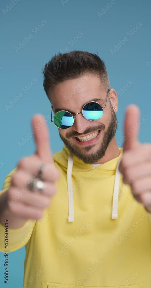 handsome casual man wearing sunglasses, smiling and giving a thumbs up with both hands handsome casual man wearing sunglasses, smiling and giving a thumbs up with both hands