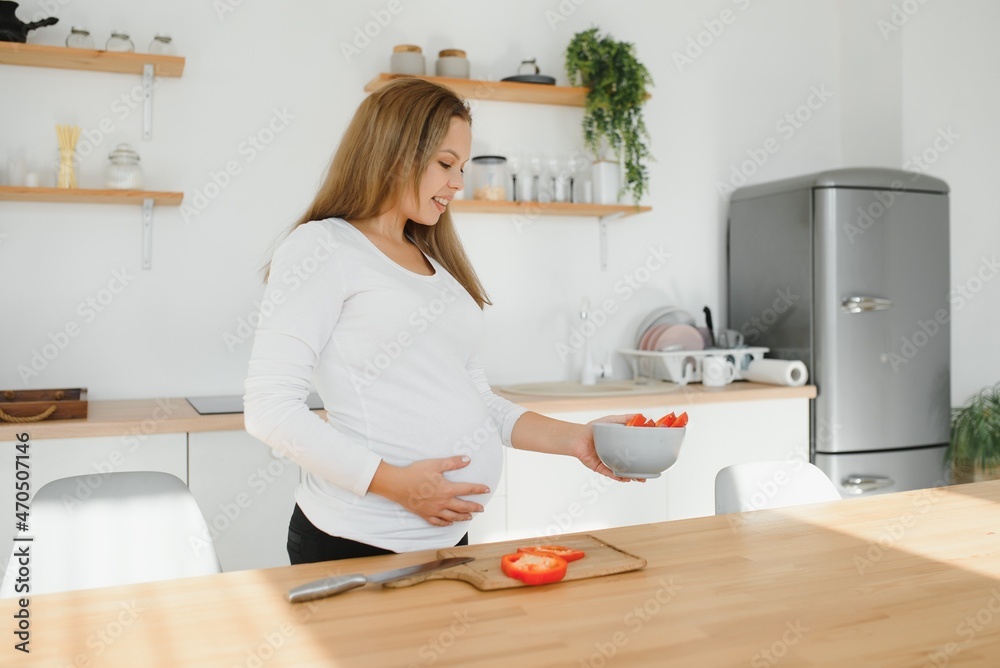 pregnancy, cooking food, healthy lifestyle, people and expectation concept - happy pregnant woman with knife chopping cucumber and preparing vegetable salad at home pregnancy, cooking food, healthy lifestyle, people and expectation concept - happy pregnant woman with knife chopping cucumber and preparing vegetable salad at home