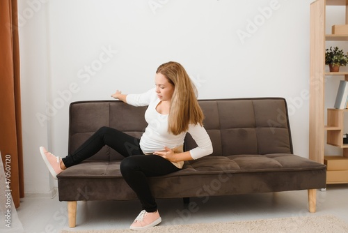 Pregnant woman getting up from sofa with hand on hip at home