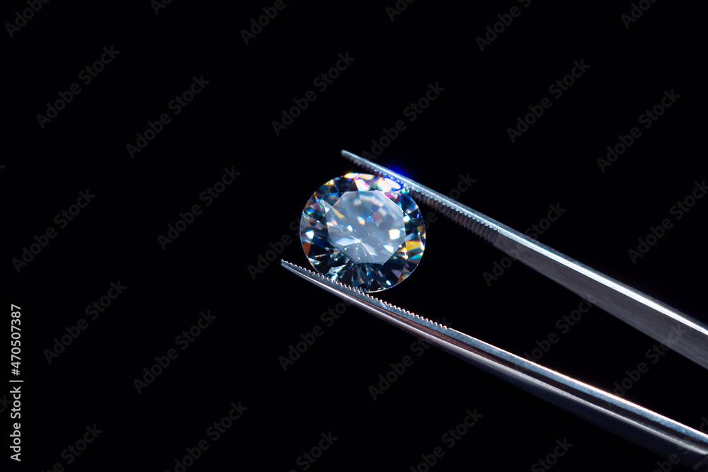 Diamond selective focus held in metal jeweller tweezers, brilliant stone cut inspection of polish quality and contamination. Natural carbon material, for industrial and fashion applications. Diamond selective focus held in metal jeweller tweezers, brilliant stone cut inspection of polish quality and contamination. Natural carbon material, for industrial and fashion applications.