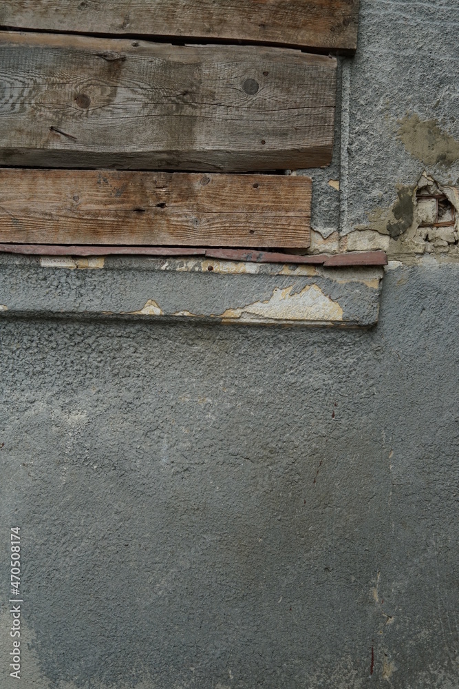 The wall of the house with peeling plaster. Texture of the ancient wall of the house. The window is boarded up with wooden boards. The wall of the house with peeling plaster. Texture of the ancient wall of the house. The window is boarded up with wooden boards.