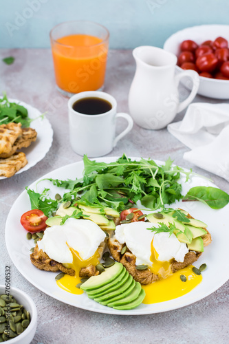 Healthy breakfast. Poached eggs on toast with avocado pieces, arugula, mizuna and chard leaves and cherry tomatoes on a plate on a served table. Flexetarian diet. Vertical view