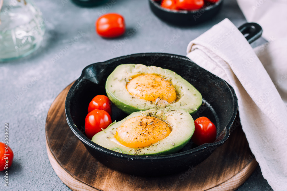 Raw avocado halves, ready to bake, stuffed with egg and cherry tomatoes in a pan on the table. Healthy eating. Flexitarian diet Raw avocado halves, ready to bake, stuffed with egg and cherry tomatoes in a pan on the table. Healthy eating. Flexitarian diet