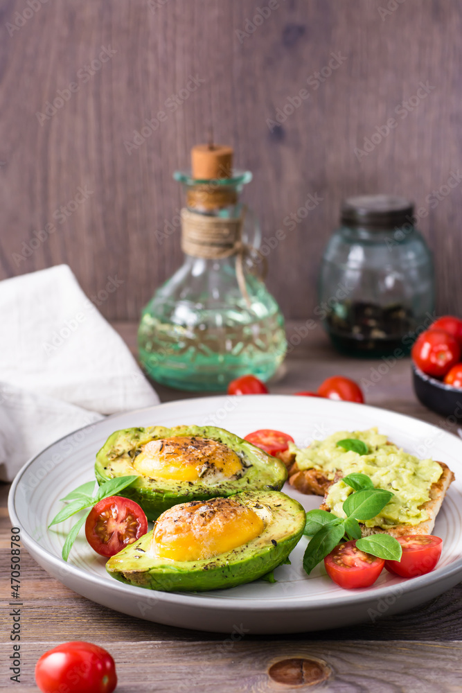 Hot appetizer baked avocado with egg, toast, cherry tomatoes and basil on a plate on a wooden table. Healthy eating. Flexitarian diet. Vertical view