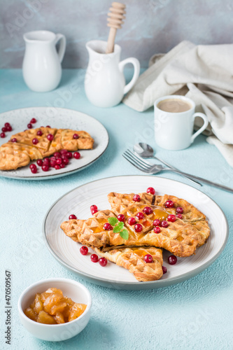 Crispy croffles with red currants, honey and mint on plates, a cup of coffee and jam on a light table. Sweet delicious breakfast. Vertical view