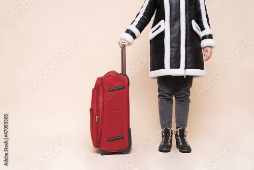 Woman in the warm clothes with a red traveling bag on the light background with copy space.