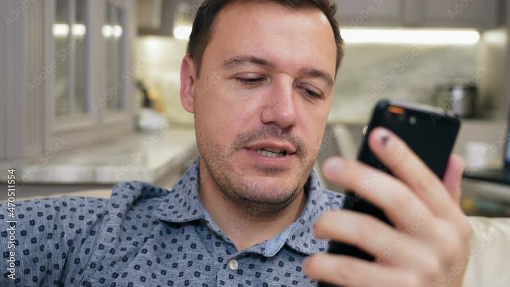 Millennial man sitting on sofa at home and looking at camera on mobile phone make live video conference call, videochat concept