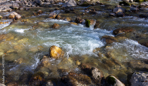 Autumn morning on a mountain river, a shallow riverbed with clear water and the rays of the sun illuminating the rocky bottom.