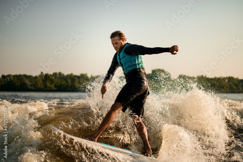 wet man energetically balancing on wave on wakesurf board.