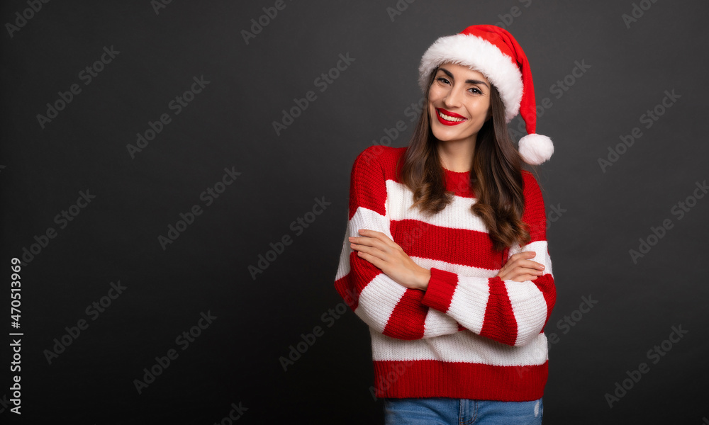 Close up photo of an attractive happy young brunette woman in Christmas hat with crossed hands and posing isolated on gray background Close up photo of an attractive happy young brunette woman in Christmas hat with crossed hands and posing isolated on gray background