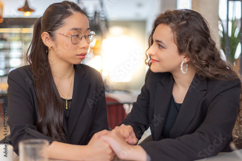 Fototapeta Dos mujeres de negocios, asiática y caucásica, se miran y se cogen las manos